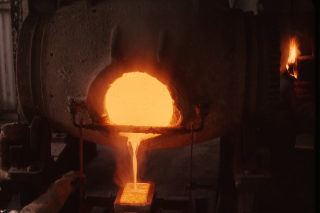 Aus der glühenden Öffnung eines Schmelzofens fließt flüssiges Gold in eine Barrenform