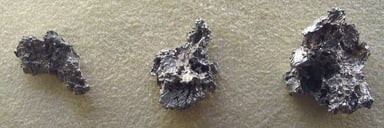 Drei unregelmäßig geformte, silbergraue Platin‑Nuggets mit rauer, löchriger Oberfläche auf hellem Filz