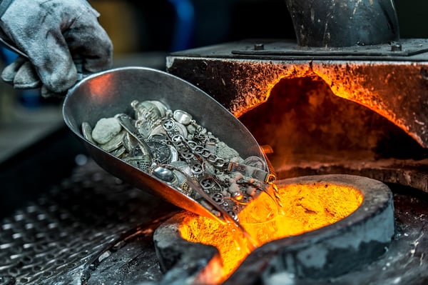 Altsilber, Münzen und Schmuckteile rutschen von einer Schaufel in einen glühenden Tiegel