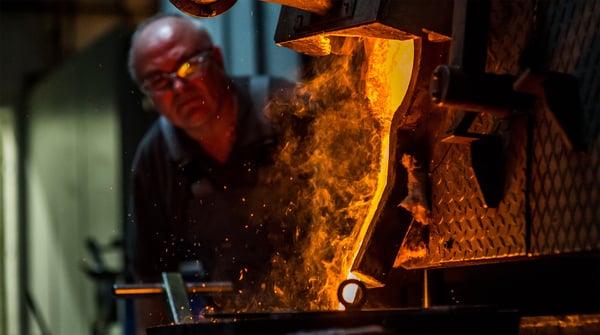 Ein Schmelzer gießt flüssiges Metall aus dem Tiegel, Funken sprühen