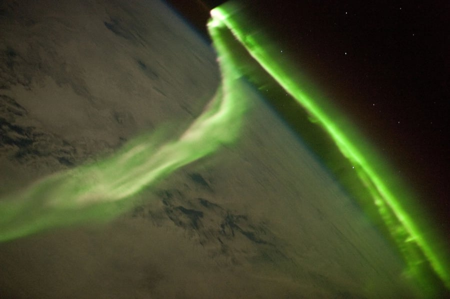 Green aurora as a glowing band above the dark Earth, seen from the space station